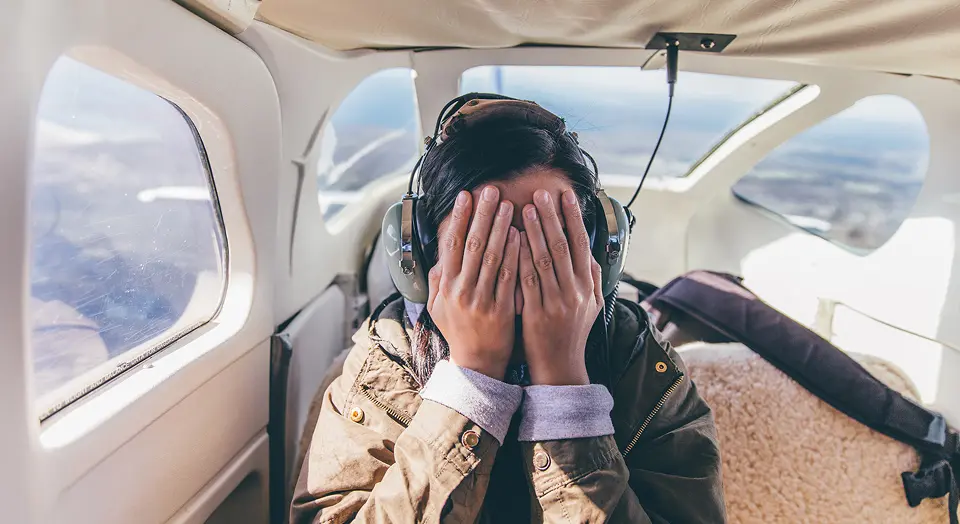 Frau sitzt mit Händen vor dem Gesicht in einem Flugzeug