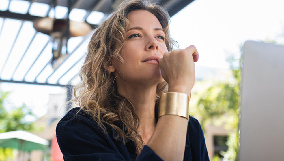 Blonde Frau in schwarzem Hemd sitzt in einem Cafè und arbeitet am Laptop