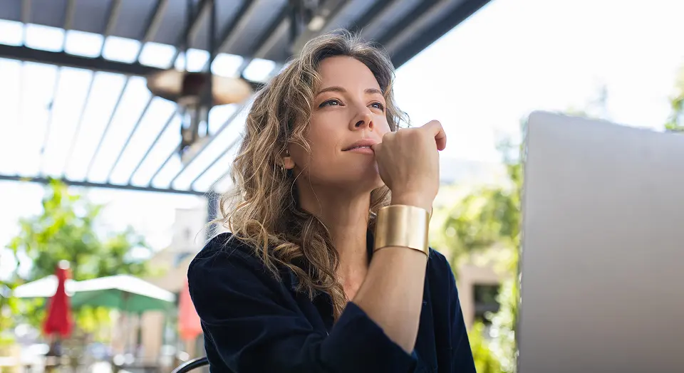 Blonde Frau in schwarzem Hemd sitzt in einem Cafè und arbeitet am Laptop