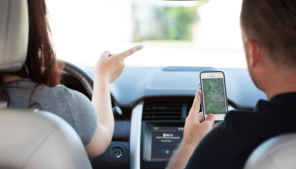 Mann und Frau sitzen in einem Auto und haben das Navigationssystem am Handy angeschaltet