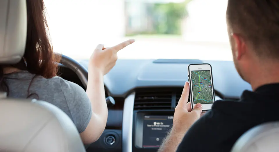 Mann und Frau sitzen in einem Auto und haben das Navigationssystem am Handy angeschaltet