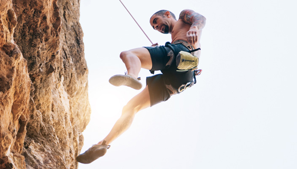 Mann in Sportklamotten klettern einen Berg herunter und ist dabei mit einem Seil gesichert