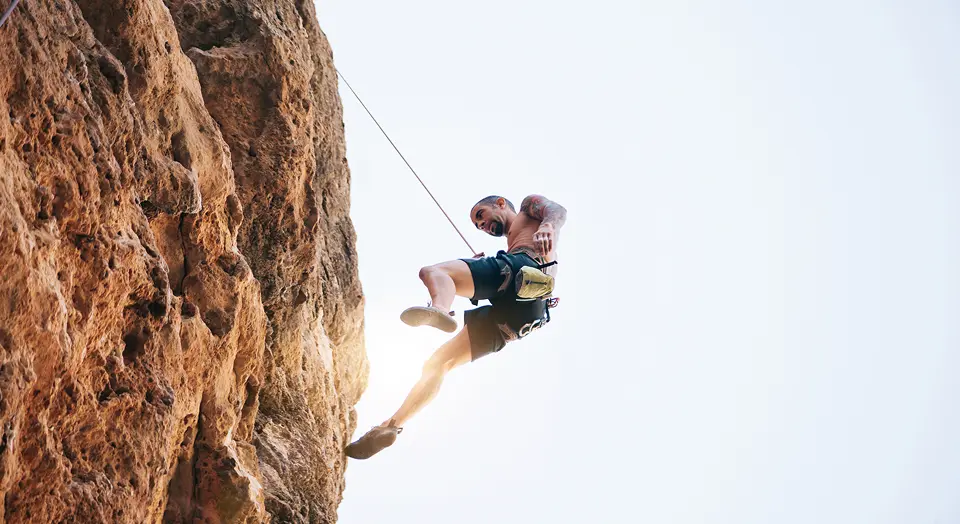Mann in Sportklamotten klettern einen Berg herunter und ist dabei mit einem Seil gesichert