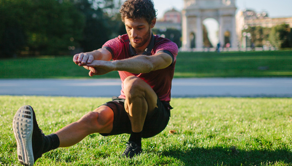 Mann in Sportklamotten treibt Sport auf einer Wiese im Freien