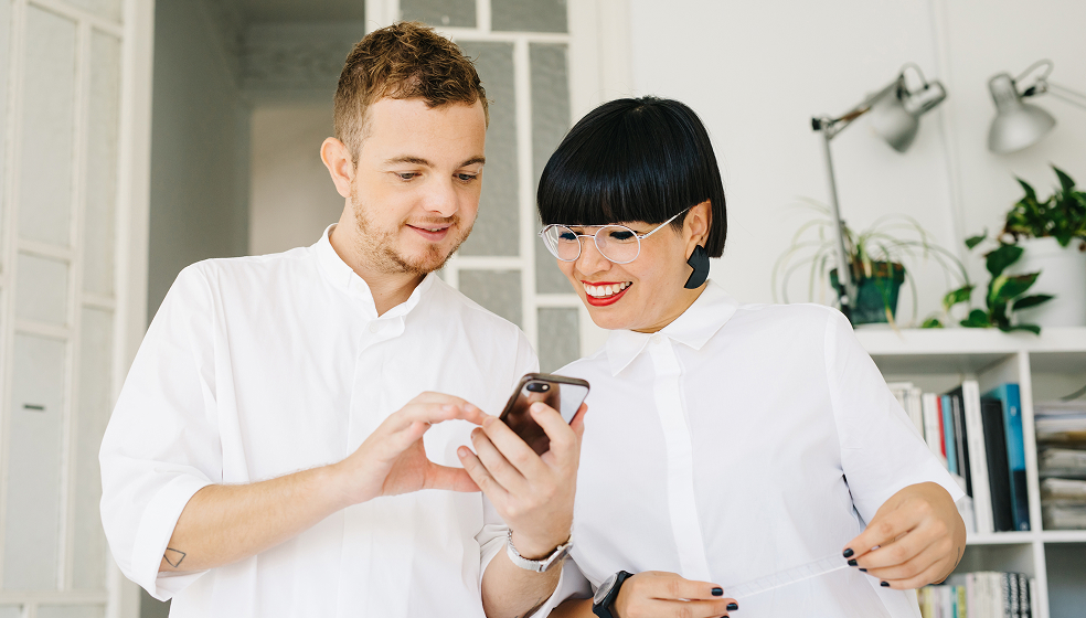 Mann und Frau in weißen Hemden schauen in ein Smartphone
