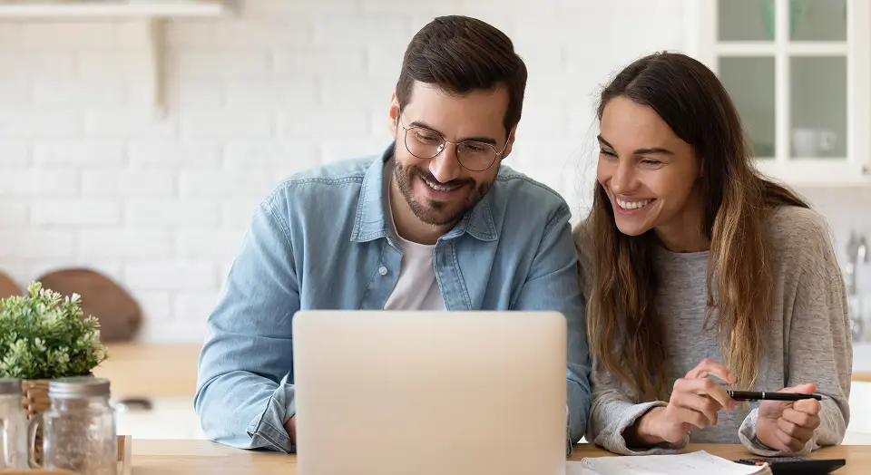 Frau und Mann sitzen in der Küche nebeneinander und schauen in einen Laptop