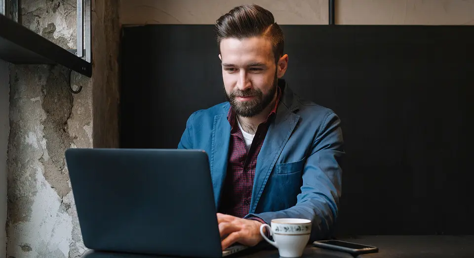 Mann in blauem Sakko sitzt in einem Café und arbeitet an seinem Laptop