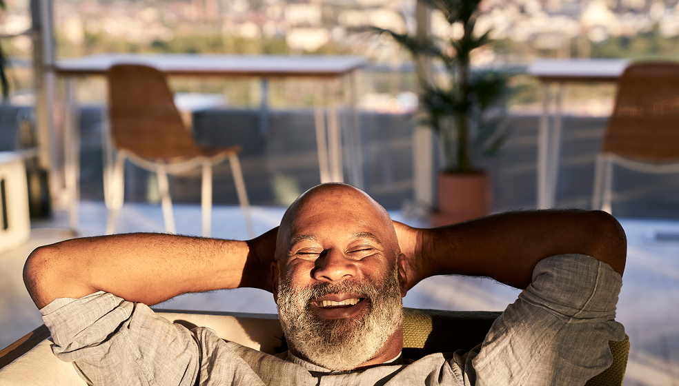 Mann mit Vollbart liegt entspannt mit Händen hinter dem Kopf auf seinem Sofa