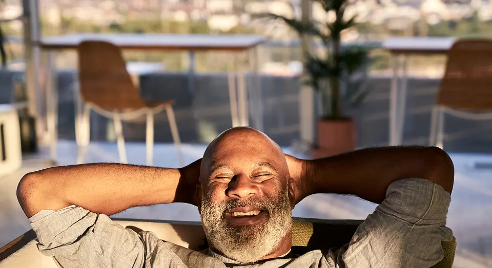 Mann mit Vollbart liegt entspannt mit Händen hinter dem Kopf auf seinem Sofa