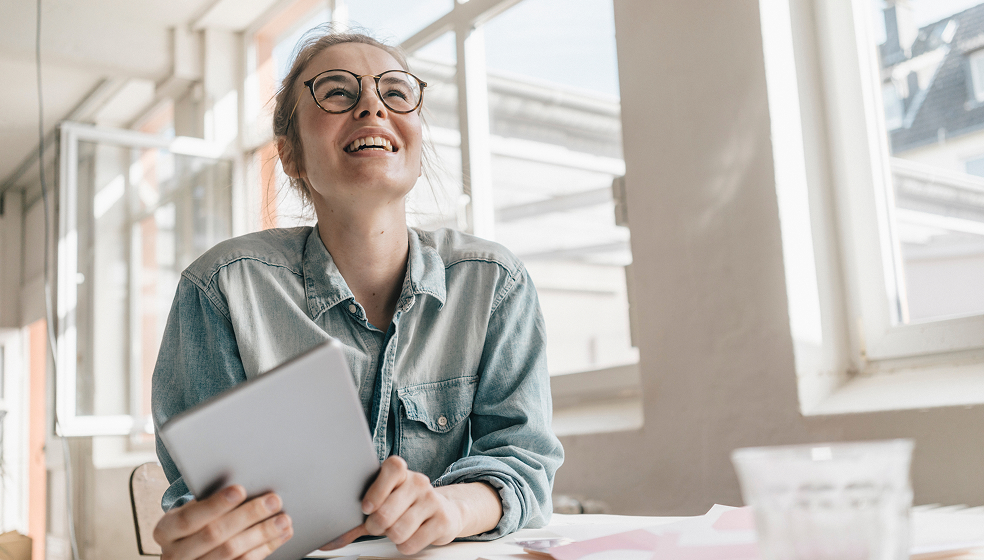 Frau mit runter Brille in Jeanshemd schaut nach oben und lächelt