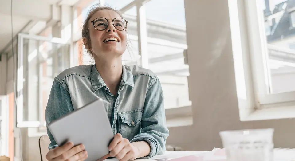 Frau mit runter Brille in Jeanshemd schaut nach oben und lächelt