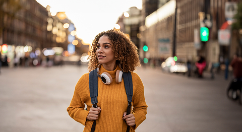 Frau in orangenem Pulli mit Rucksack auf dem Rücken läuft durch eine Stadt