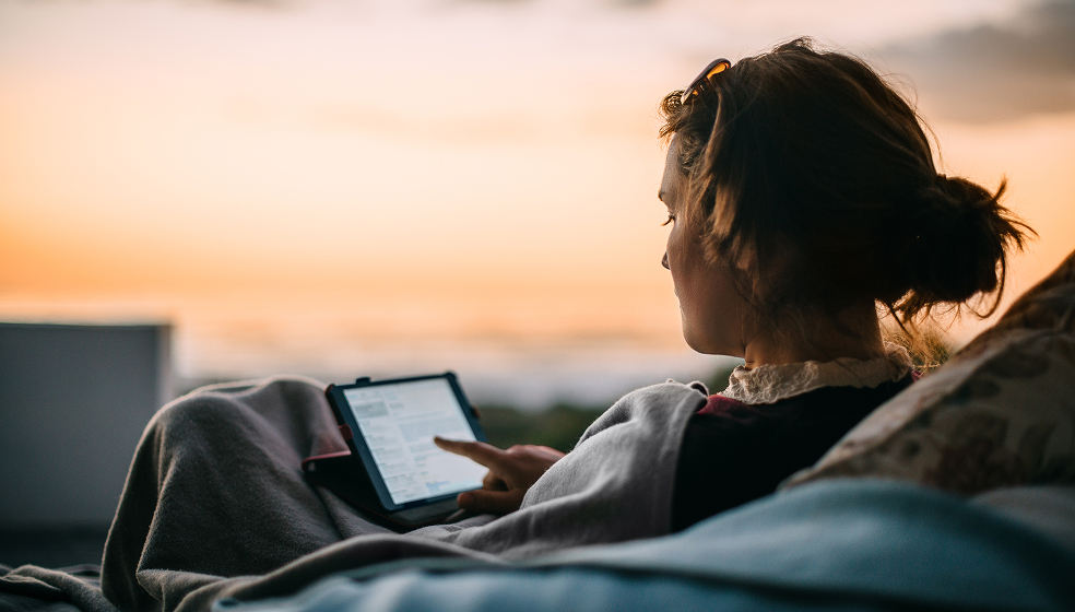 Frau sitzt im Abendrot auf ihrer Terrasse und tippt an ihrem Tablet herum