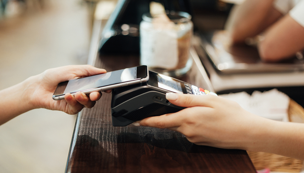 Nahaufnahme eines Smaprthones, das zum kontaktlosen Bezahlen an ein EC-Kartenzahlgerät gehalten wird