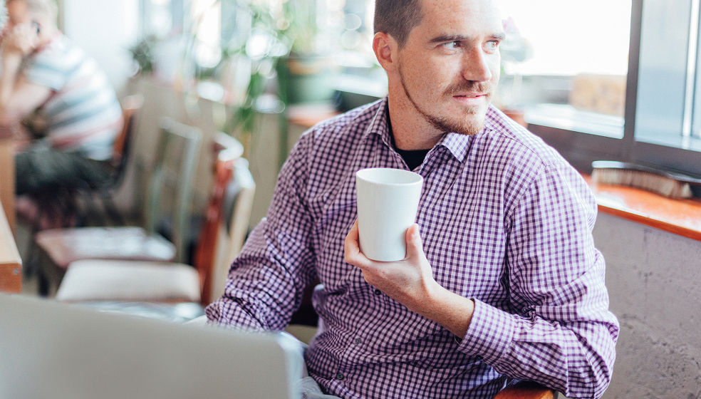 Mann in kariertem Hemd sitzt in einem Café und schaut nach draußen