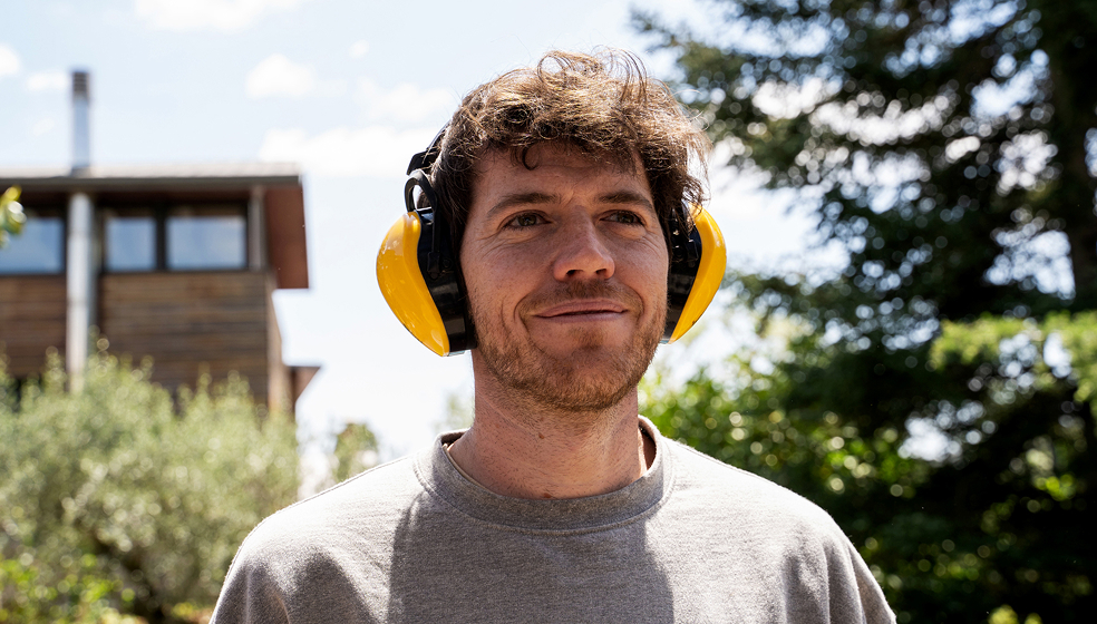 Mann mit gelben Lärmschutzkopfhörer lächelt und schaut dabei in die Ferne