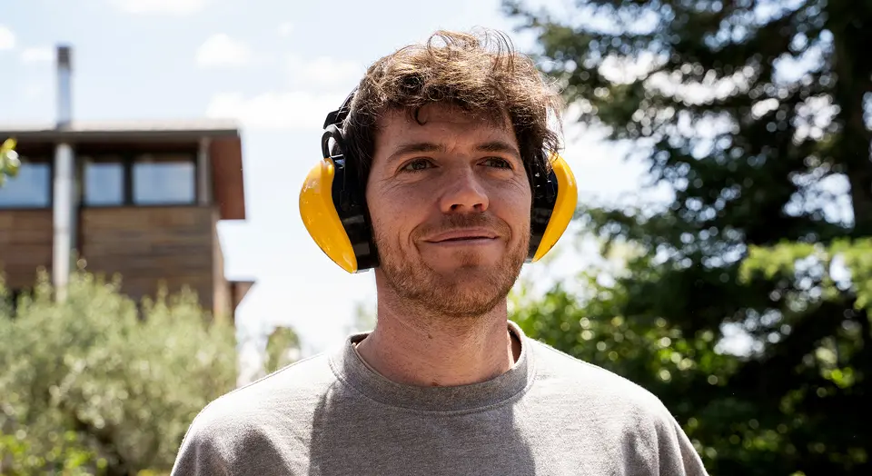 Mann mit gelben Lärmschutzkopfhörer lächelt und schaut dabei in die Ferne