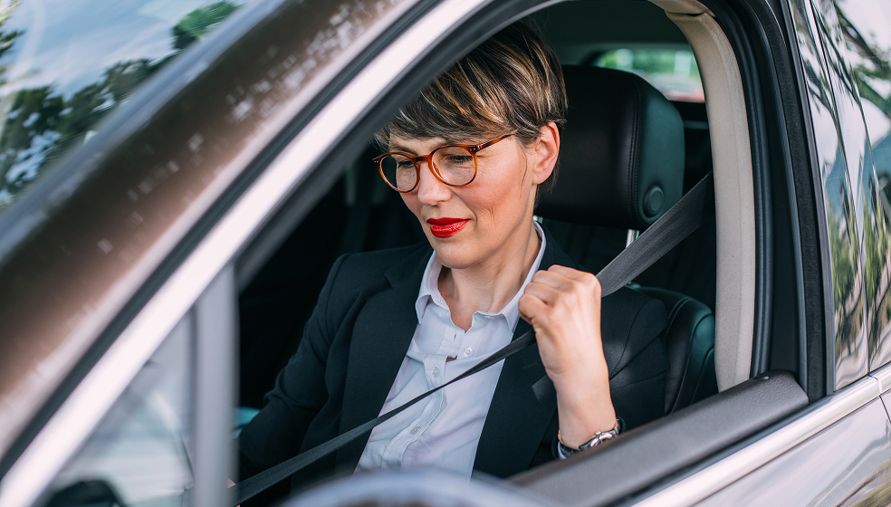 Frau in Hemd und Blazer sitzt angeschnallt im Auto