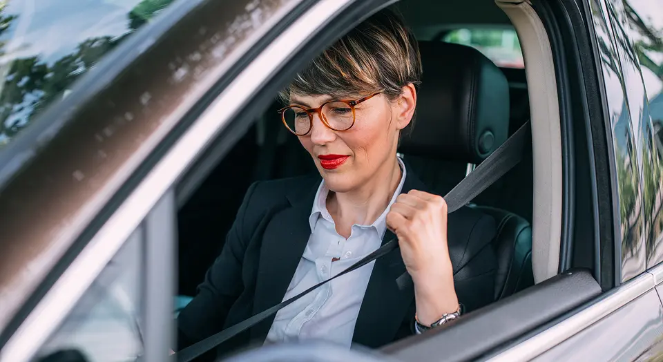 Frau in Hemd und Blazer sitzt angeschnallt im Auto