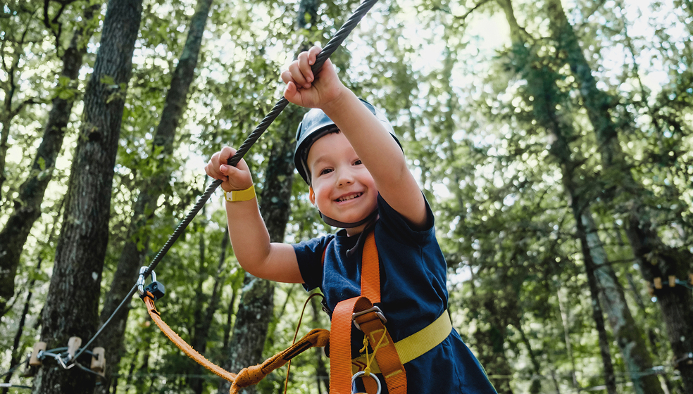 Kind mit Helm klettert gesichert durch einen Hochseilgarten