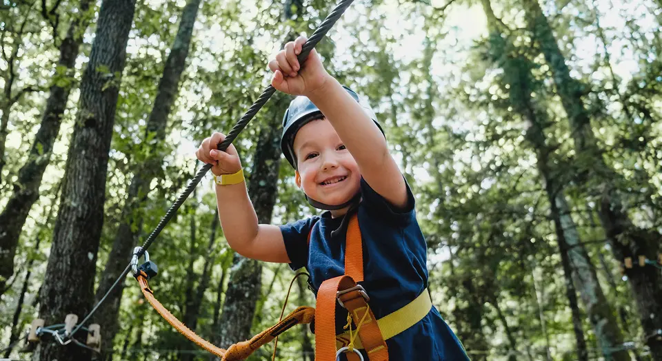 Kind mit Helm klettert gesichert durch einen Hochseilgarten