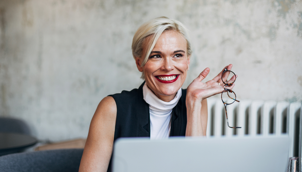 Blonde Frau sitzt vor ihrem Laptop und schaut in die Ferne