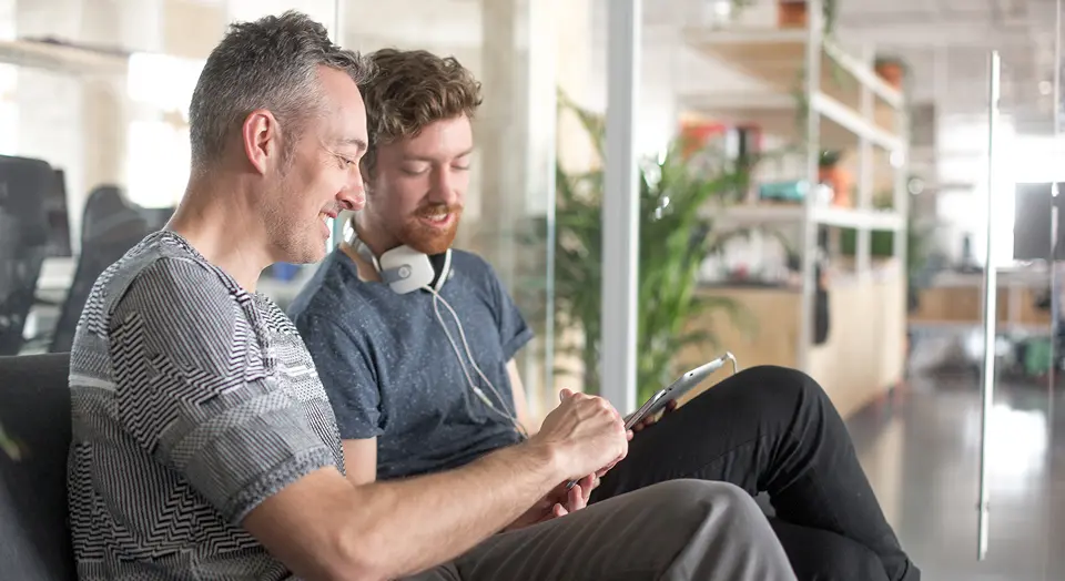 Zwei Männer sitzen im Büro nebeneinander und schauen gemeinsam in ein Tablet