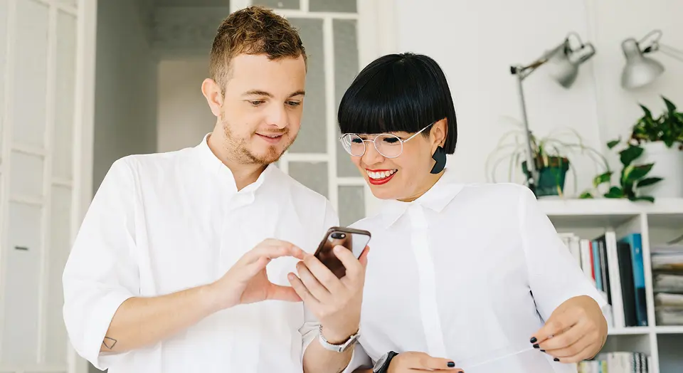 Mann und Frau in weißen Hemden schauen gemeinsam in ein Smartphone