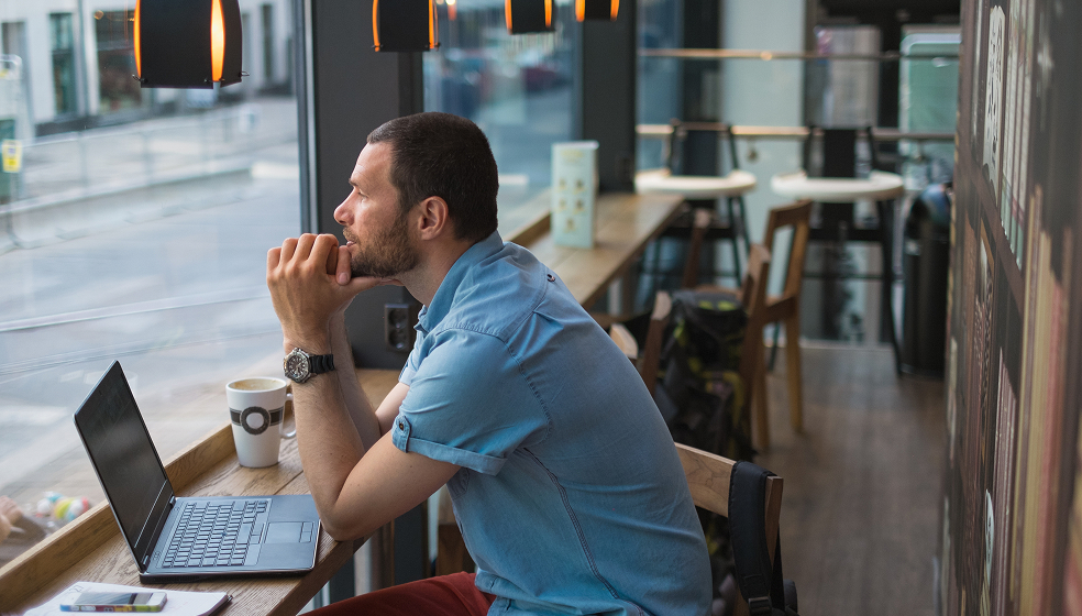 Mann in blauem Hemd sitzt in einem Café und schaut nach draußen