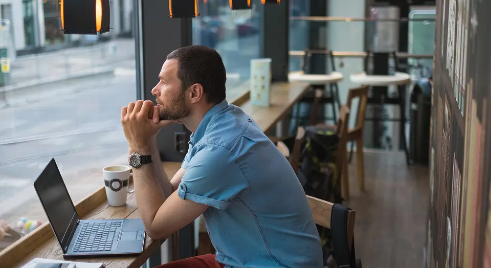 Mann in blauem Hemd sitzt in einem Café und schaut nach draußen