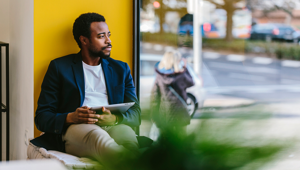 Mann sitzt in einem Café im Fenster vor einer gelben Wand und schaut nach draußen