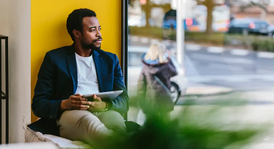 Mann sitzt in einem Café im Fenster vor einer gelben Wand und schaut nach Draußen