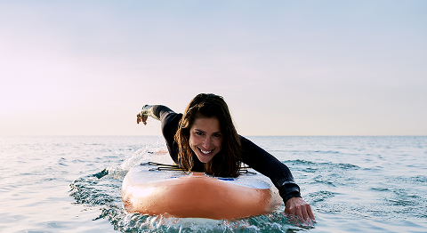 Frau in Neoprenanzug liegt im Meer auf einem Stand-Up Paddle