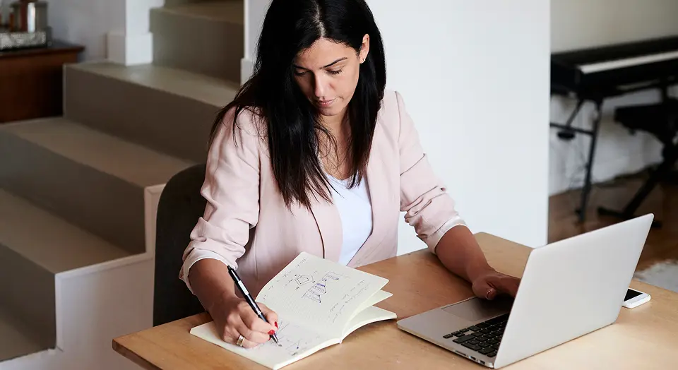 Dunkelhaarige Frau in rosanem Blazer macht ihr Steuererklärung mit Laptop und Notizbuch
