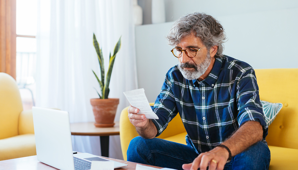 Mann in kariertem Hemd sitzt auf einem gelben Sofa und schaut sich einen Notizzettel an