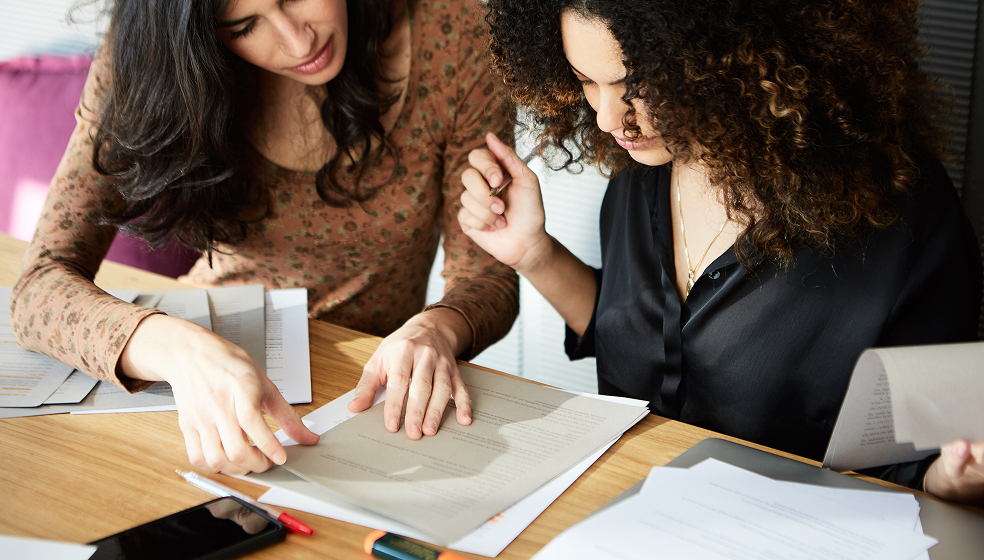 Zwei Frauen sitzen an einem Tisch und schauen sich gemeinsam Dokumente an