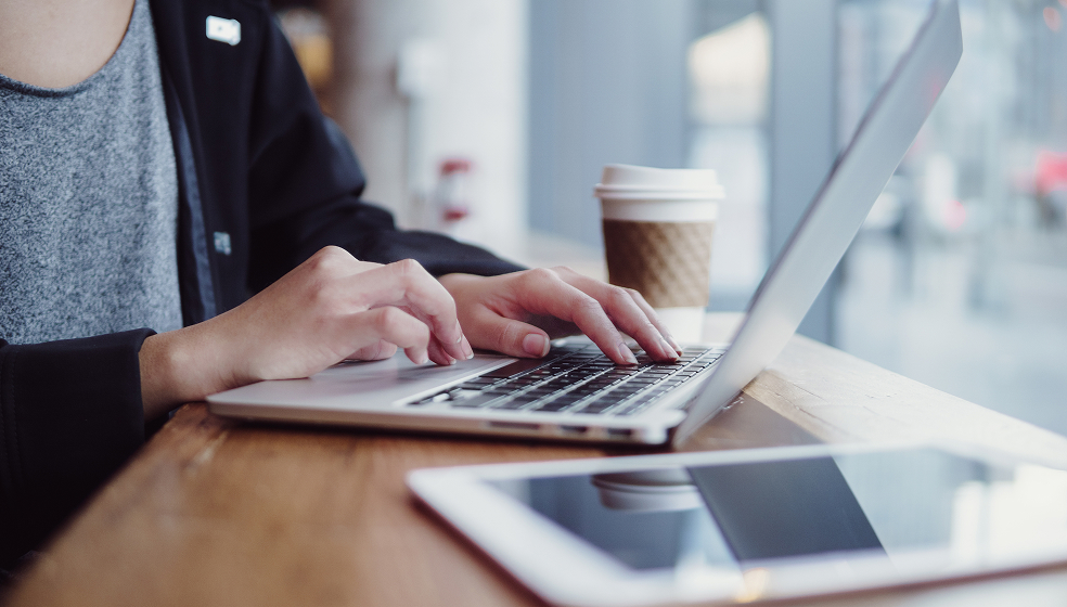 Nahaufnahme eines Mannes, der in einem Café an seinem Laptop arbeitet