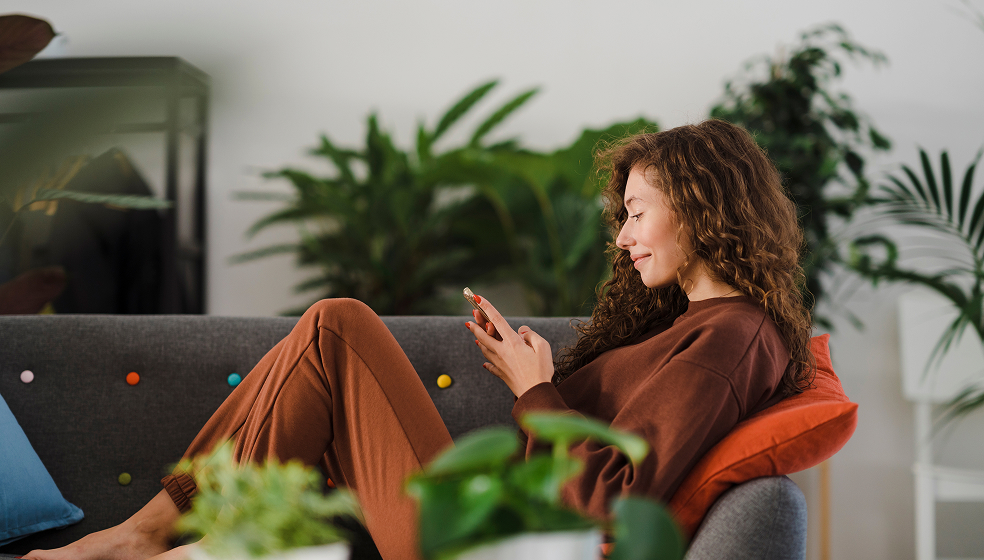 Lockige Frau liegt auf dem Sofa und schaut in ihr Smartphone