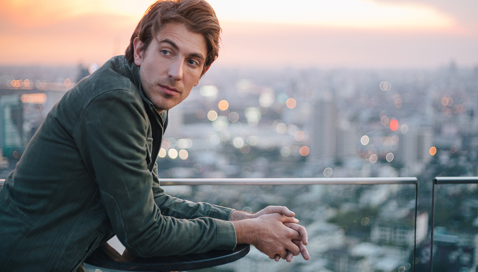 Mann in Sakko steht auf einer Dachterrasse und schaut in die Ferne