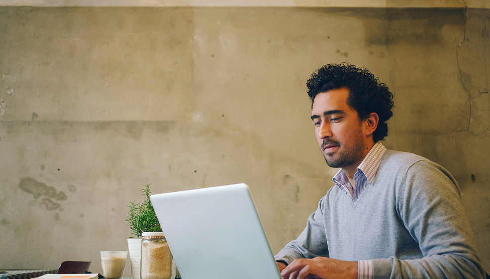 Dunkelhaariger Mann sitzt vor einer goldenen Wand an seinem Laptop