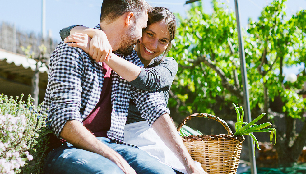 Pärchen sitzt im Grünen und umarmt sich glücklich