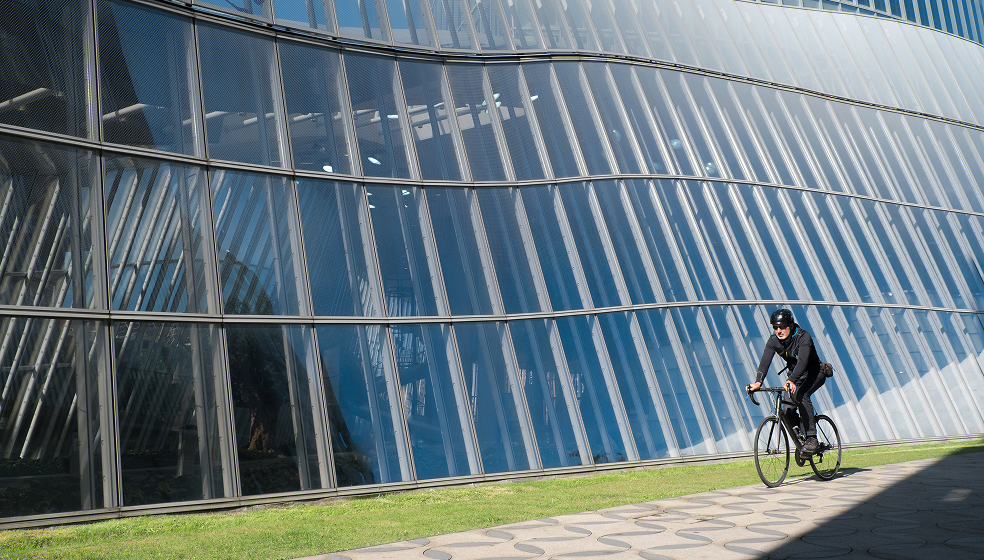 Mann fährt Fahrrad vor einem Glasgebäude