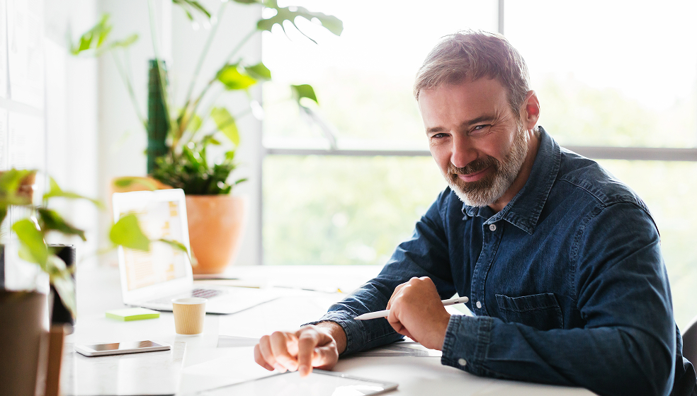 Mann in Hemd arbeitet an seinem Schreibtisch und lächelt