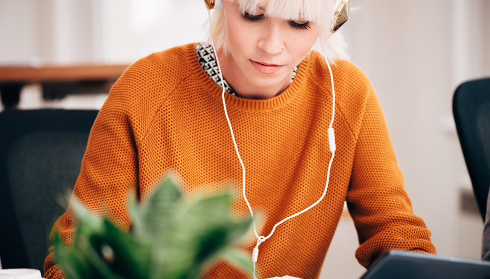 Blonde Frau in orangenem Pullover arbeitet mit Kopfhörern in den Ohren