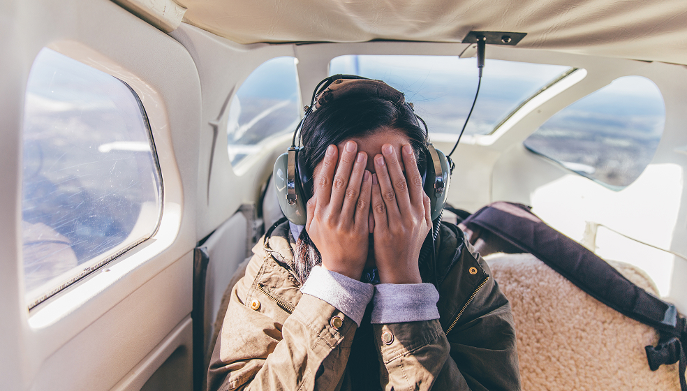 Frau sitzt in kleinem Flugzeug und hält sich die Augen zu