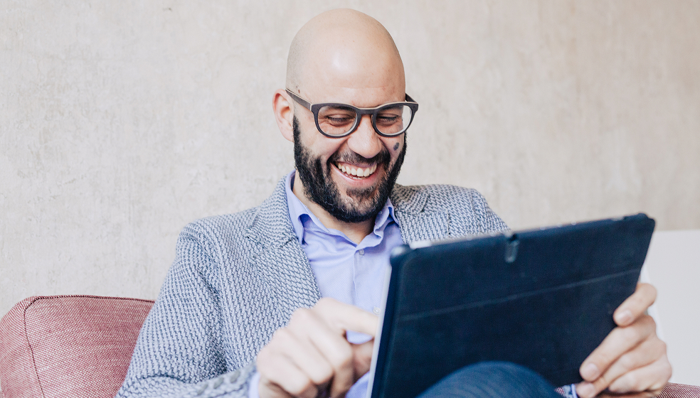Mann in Businessklamotten sitzt vor seinem Tablet und lacht