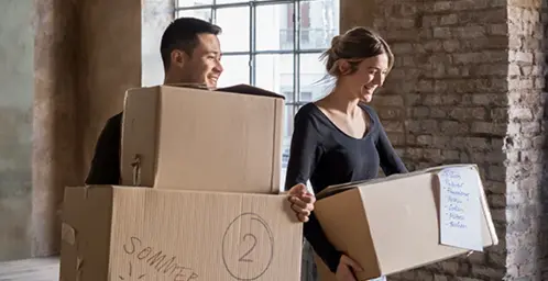Mann und Frau tragen Umzugskartons in einem leeren Haus