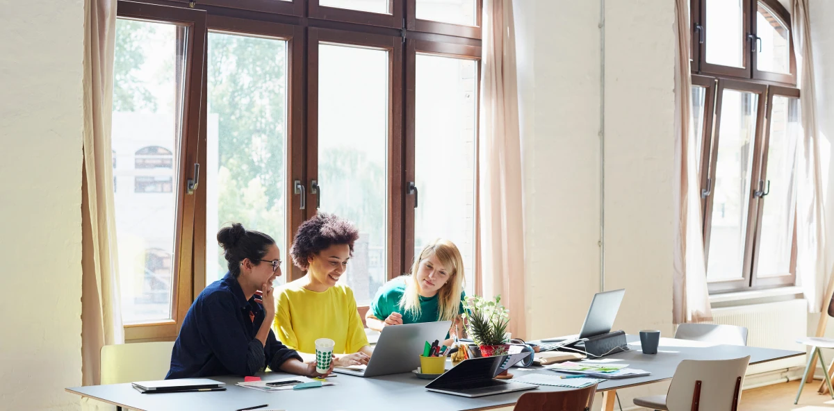 Drei Frauen sitzen um einen Laptop herum und arbeiten an einem Projekt