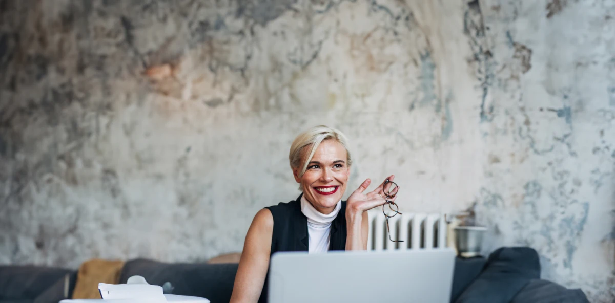 Blonde Frau hält ihre Brille in der Hand und lächelt