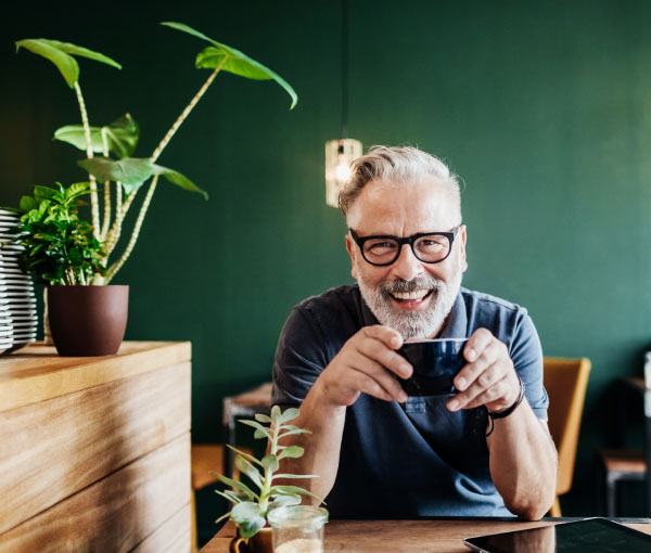 Mann mit grauen Haaren und schwarzer Brille trinkt Kaffee